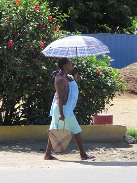 Mosambik, Frau unterwegs mit Sonnenschirm und Kind im Tragetuch