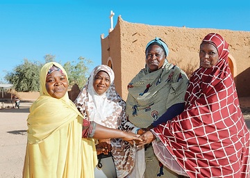 Christliche und muslimische Frauen reichen sich vor der Lehmkirche der Gemeinde Saint Augustin in Agadez (Niger) als Zeichen des Friedens symbolisch die Hand. Auf die Kirche wurde 2016 ein Brandanschlag verübt. Die Lehmarchitektur der Stadt gehört seit Juni 2013 zum UNESCO Welterbe.